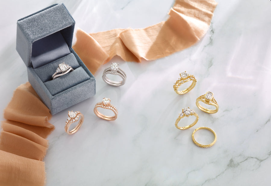 Elegant diamond engagement rings in gold, rose gold, and platinum, displayed on marble with velvet box and fabric accents.
