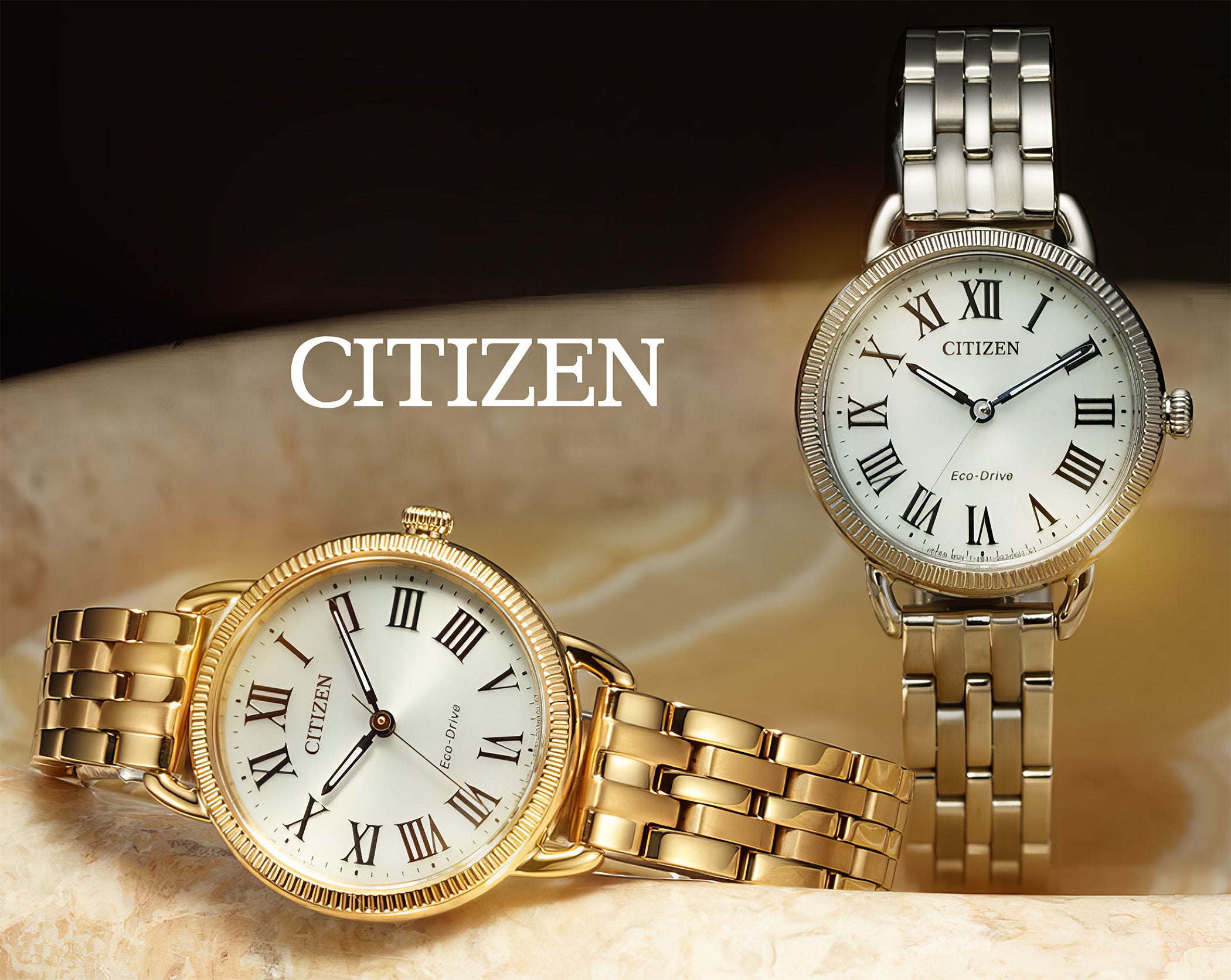 Two Citizen Eco-Drive watches with Roman numerals, one gold and one silver, on marble surface.