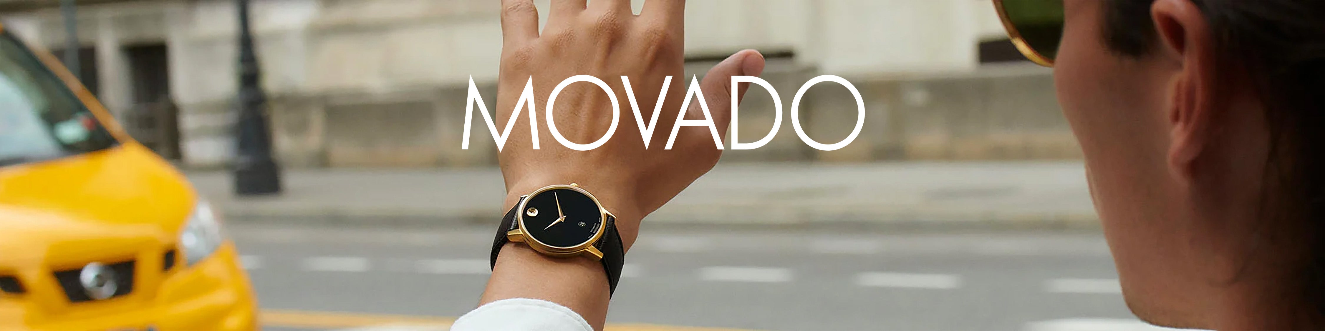 Person hailing taxi wearing black and gold Movado watch on city street