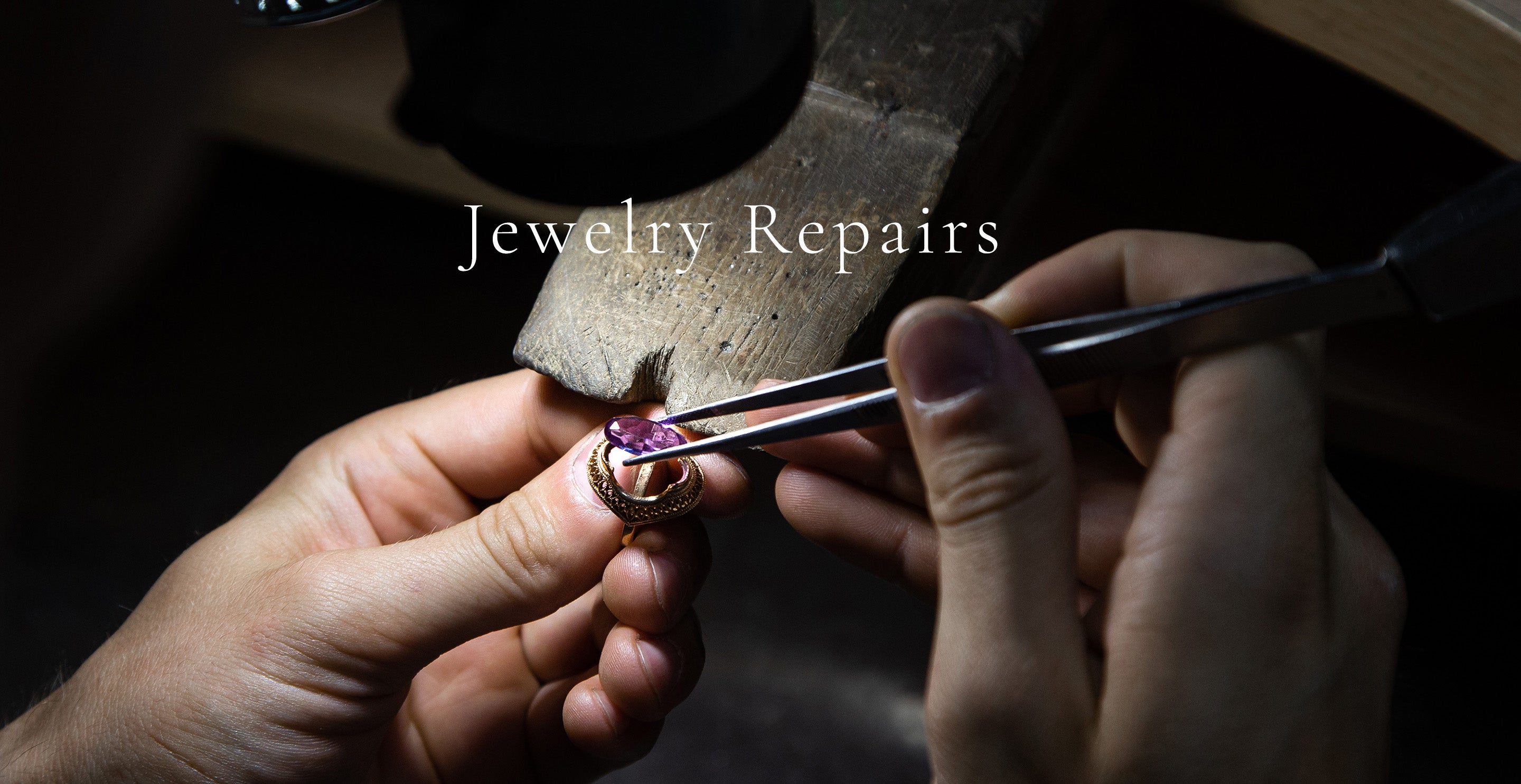 Close-up of jeweler repairing ring with pink gemstone using tweezers at workbench