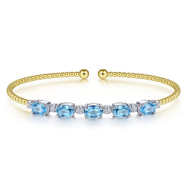 Gold cuff bracelet with blue gemstones and diamond accents on a white background