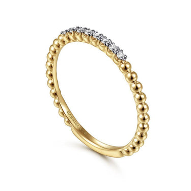 Yellow gold beaded band ring with pavé diamonds on top against white background