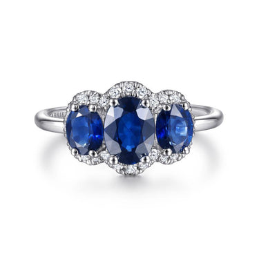 Three-stone sapphire and diamond halo ring in white gold on white background